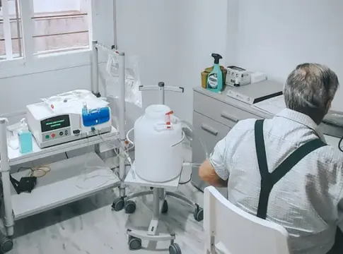 Persona junto a equipos médicos Persona sentada de espaldas junto a varios equipos médicos en una habitación luminosa