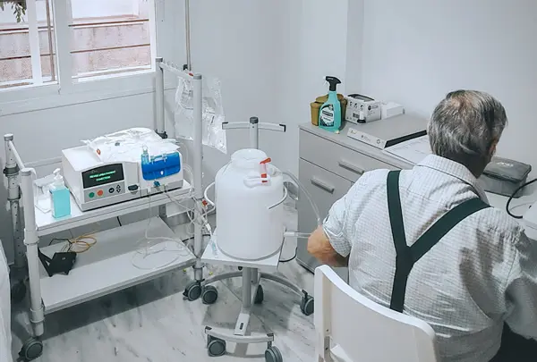 Persona sentada de espaldas junto a varios equipos médicos en una habitación luminosa