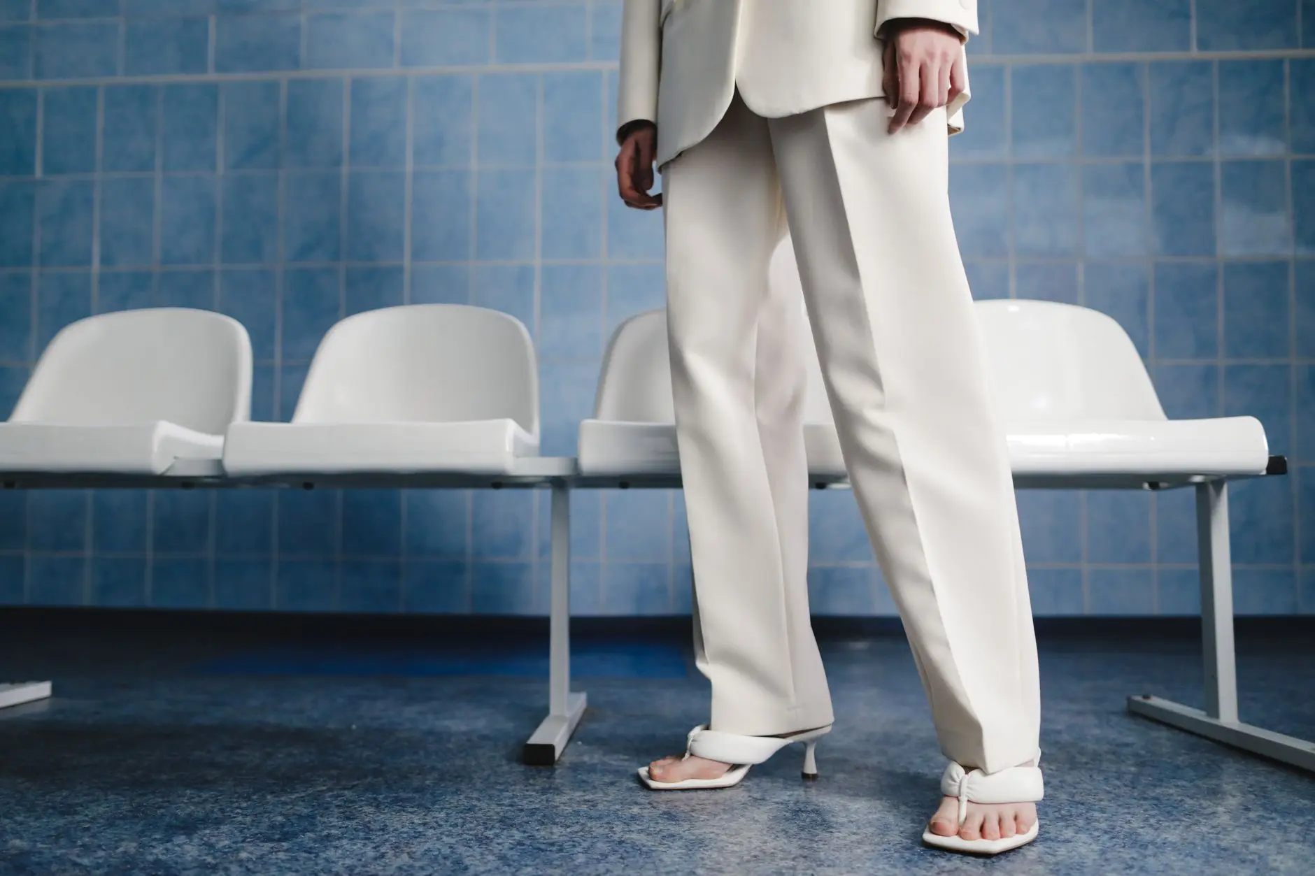 Una mujer elegante en un traje blanco y sandalias, de pie en una sala de espera moderna.