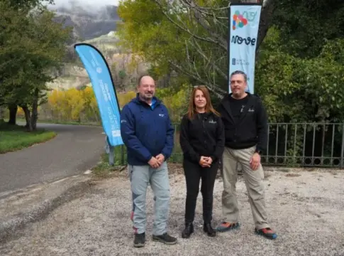 Tres personas junto a banderolas de V NOVE Tres personas posan junto a banderolas de V NOVE en un entorno arbolado.