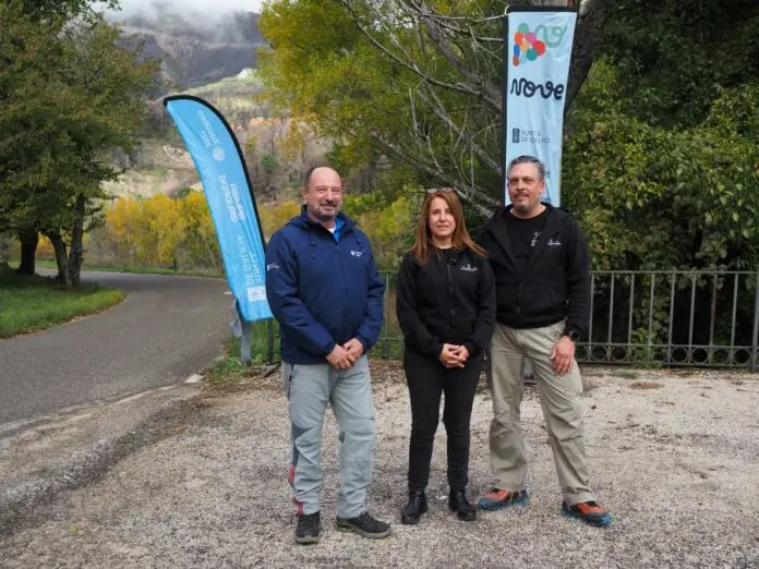 Tres personas junto a banderolas de V NOVE Tres personas posan junto a banderolas de V NOVE en un entorno arbolado.