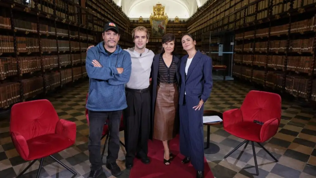 Personas en una biblioteca histórica Cuatro personas posan entre estanterías de libros antiguos y sillones rojos