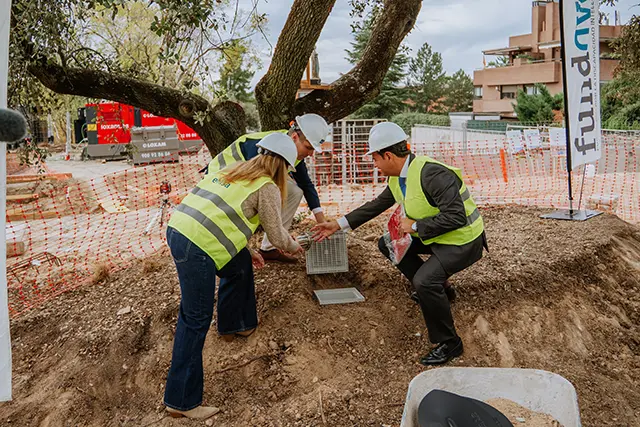 Tres personas con cascos colocan una placa en un terreno de construcción.