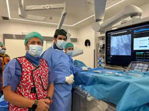 Personas en una sala de procedimientos Personas con mascarillas junto a una mesa cubierta y un monitor médico