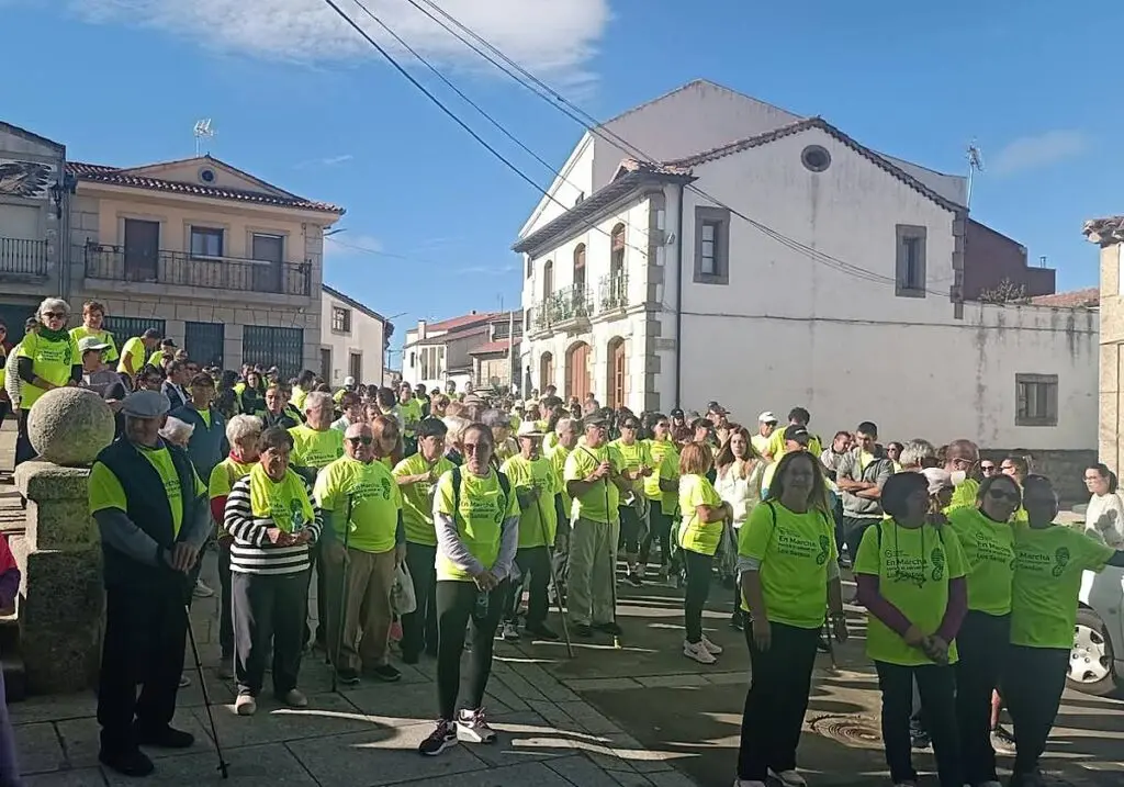 Participantes reunidos para la marcha contra el cáncer Grupo de personas con camisetas verdes reunidas en una calle del pueblo.