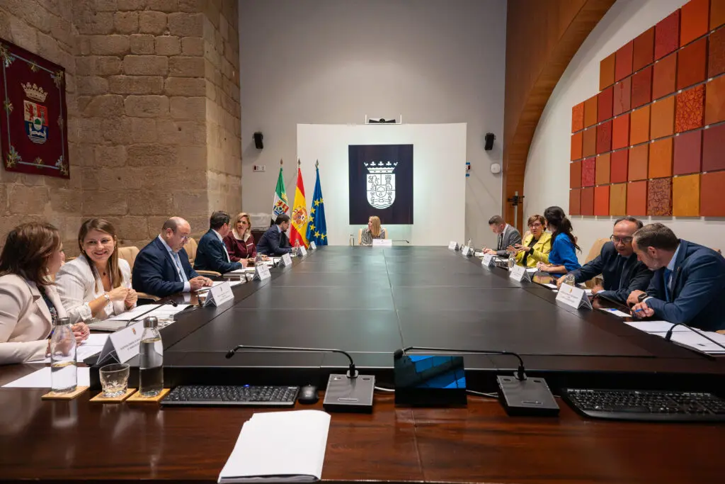 Personas sentadas alrededor de una larga mesa en una sala de reuniones institucional.