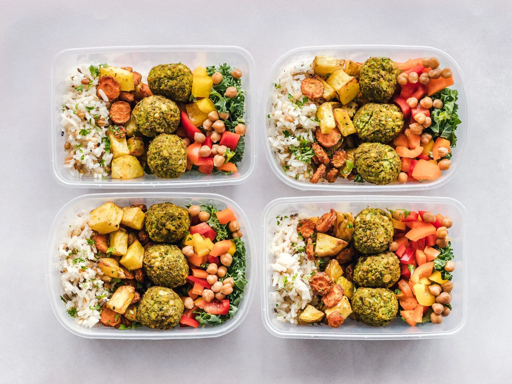 Contenedores de comida coloridos con falafel, garbanzos, arroz y verduras para un estilo de vida saludable.