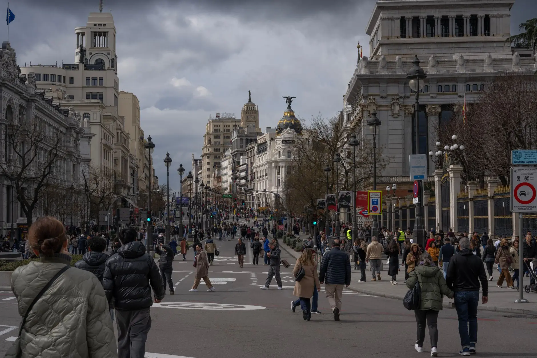 Concurrida escena callejera en el centro de la ciudad de Madrid con arquitectura icónica y peatones bulliciosos bajo un cielo nublado.