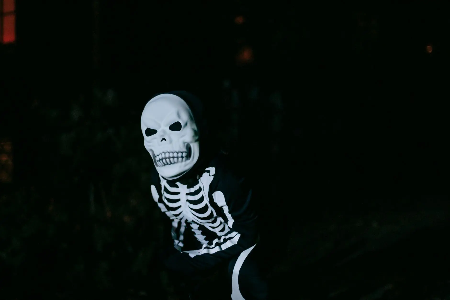 Una persona vestida con un disfraz de esqueleto posa al aire libre por la noche, celebrando Halloween.