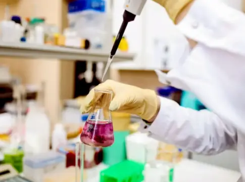 Pipeta y matraz con líquido rosa Una mano enguantada utiliza una pipeta sobre un matraz con líquido rosa en un laboratorio.