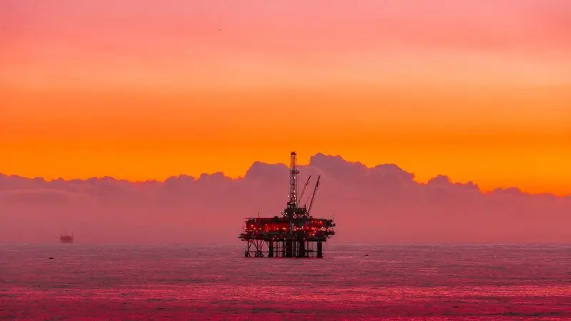 Márgenes de refino y geopolítica: por qué el coste real del petróleo supera los 140 dólares 2 Merca2 Plataforma petrolífera iluminada sobre el mar bajo un cielo naranja al atardecer. Fuente: Unsplash