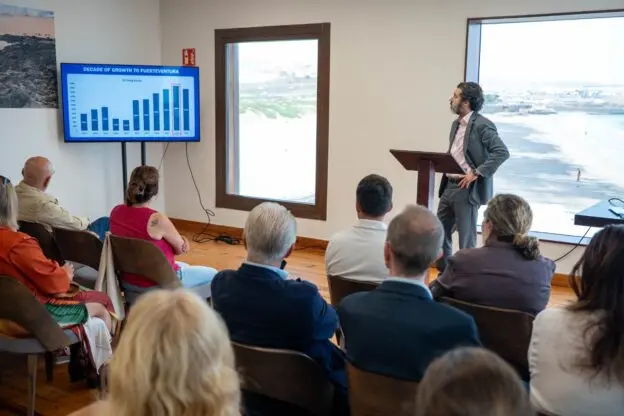 Un hombre presenta un gráfico ante varias personas sentadas en una sala.
