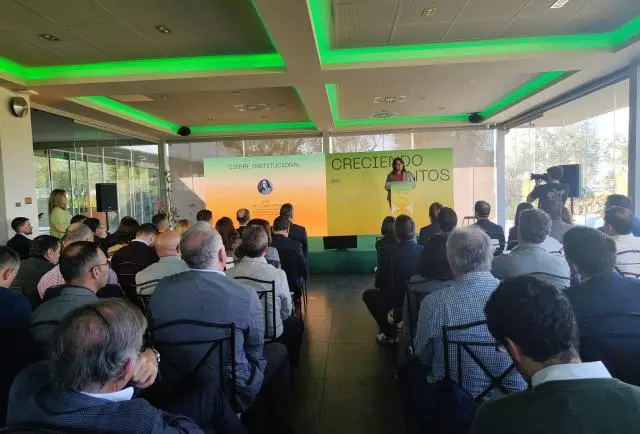 Público sentado escucha una presentación ante una pantalla con el rótulo Creciendo juntos.
