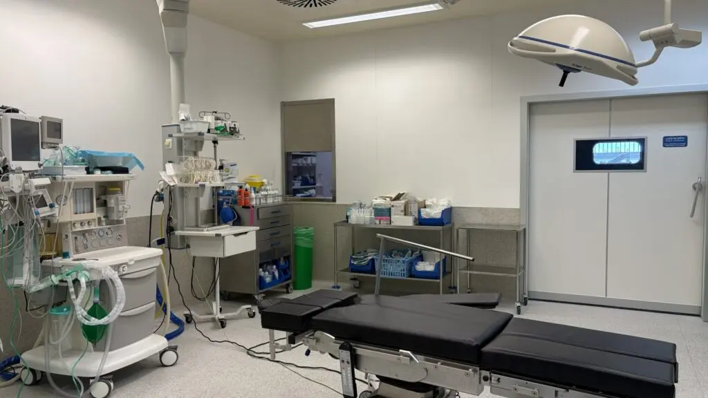 Quirófano vacío con mesa de operaciones, lámpara quirúrgica y equipos médicos.