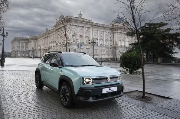Automóvil Renault 4 azul claro estacionado sobre adoquines frente a un gran edificio.