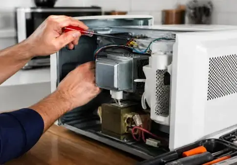 Reparación del interior de un microondas Una persona manipula con un destornillador el interior de un microondas abierto.