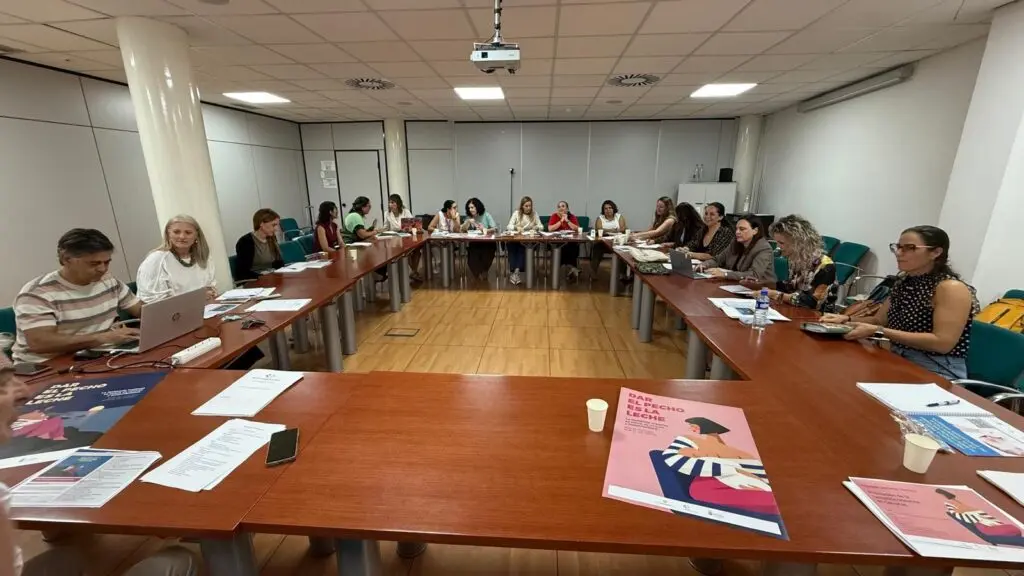 Personas reunidas alrededor de una mesa en forma de U con documentos y ordenadores portátiles