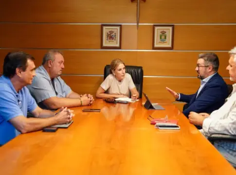 Reunión alrededor de una mesa de madera Cinco personas conversan alrededor de una mesa larga de madera en una sala.