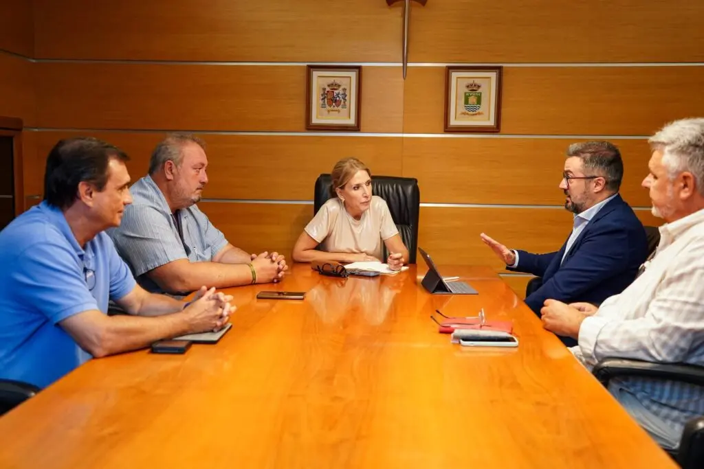 Reunión alrededor de una mesa de madera Cinco personas conversan alrededor de una mesa larga de madera en una sala.
