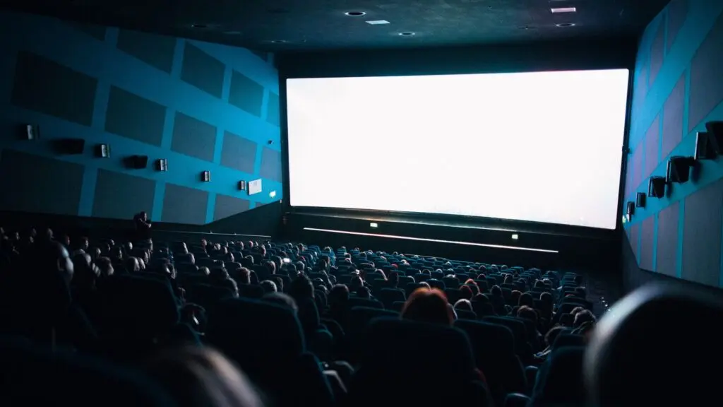 Sala de cine llena de espectadores frente a una gran pantalla iluminada.