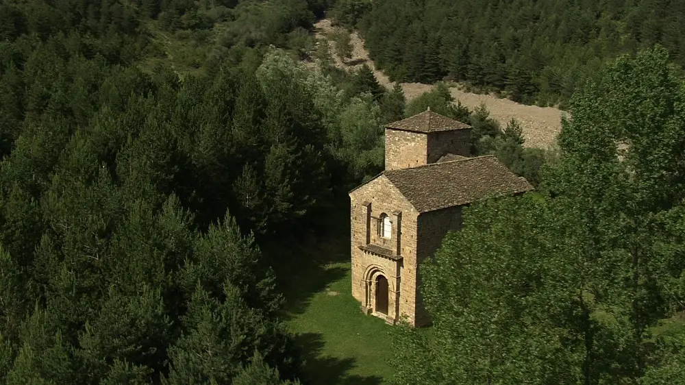 Iglesia románica de piedra rodeada de bosque, vista desde una perspectiva elevada.