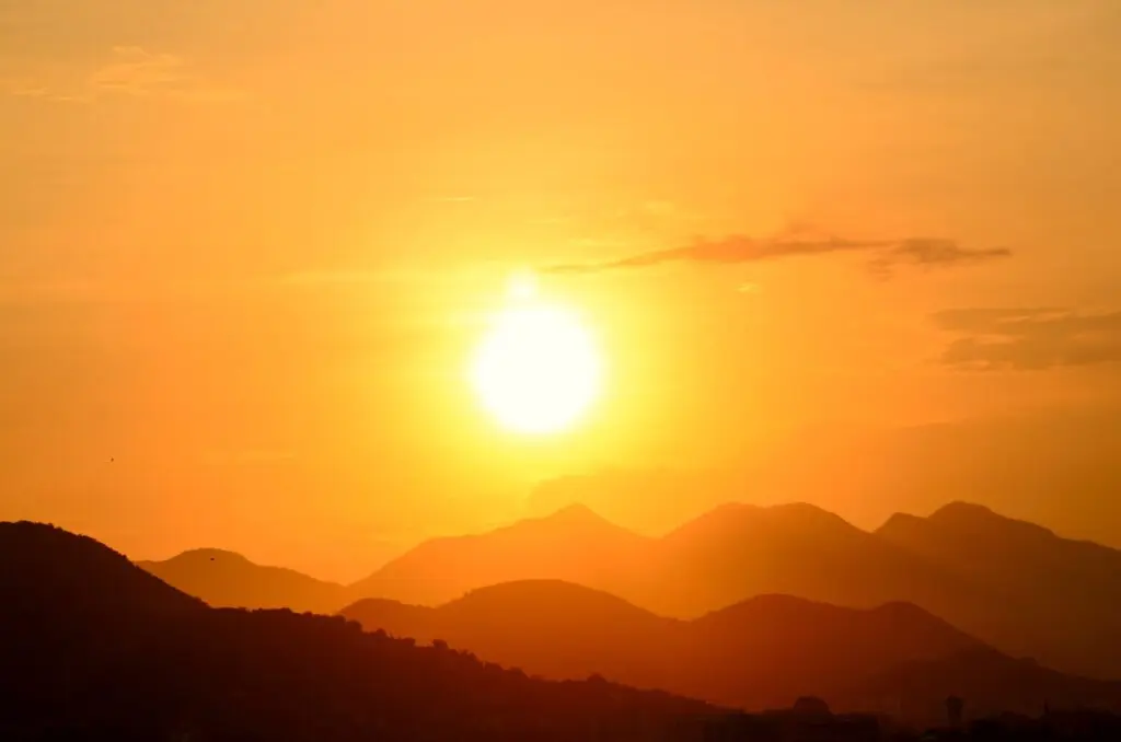El sol brillante se oculta tras varias montañas bajo un cielo anaranjado.