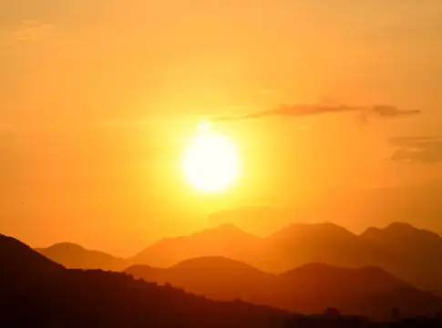 Sol bajo sobre montañas anaranjadas Sol brillante sobre un horizonte de montañas bajo un cielo anaranjado.
