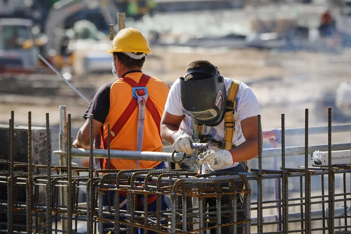 Trabajador con máscara de soldar trabaja sobre una estructura de barras metálicas en una obra