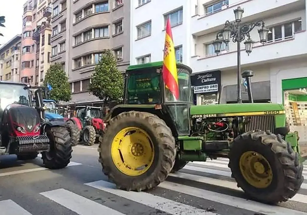 Varios tractores, incluido uno verde con bandera española, cruzan un paso de peatones.