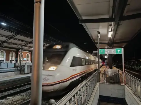 Tren en una estación nocturna Un tren blanco pasa por una estación ferroviaria iluminada durante la noche.