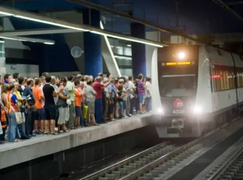 Tren de metro junto a un andén concurrido Pasajeros esperan en un andén mientras un tren de metro permanece iluminado.