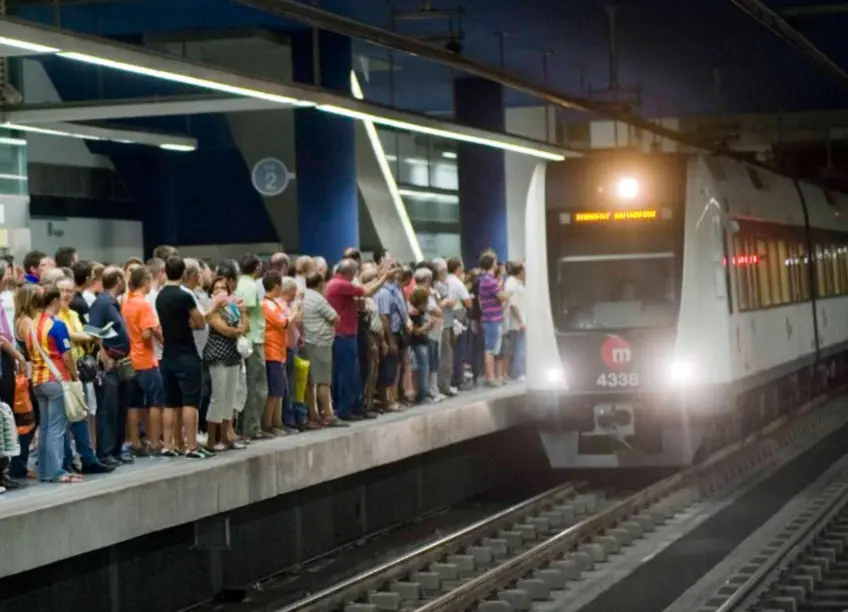 Tren de metro junto a un andén concurrido Pasajeros esperan en un andén mientras un tren de metro permanece iluminado.