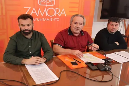 Tres hombres sentados ante una mesa con documentos y micrófonos, frente al Ayuntamiento de Zamora.