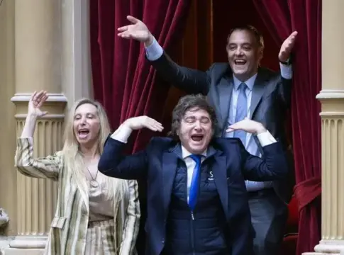Tres personas con los brazos levantados Tres personas sonríen con los brazos levantados frente a cortinas rojas.