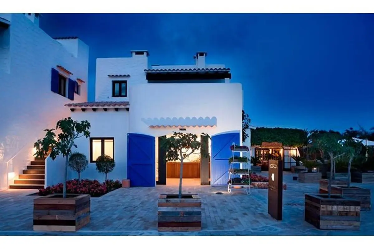 Villa blanca con puertas azules al anochecer Villa blanca de varios niveles con puertas azules y patio ajardinado al anochecer